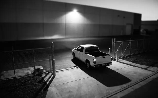 Pickup truck flagged at night beside a fence