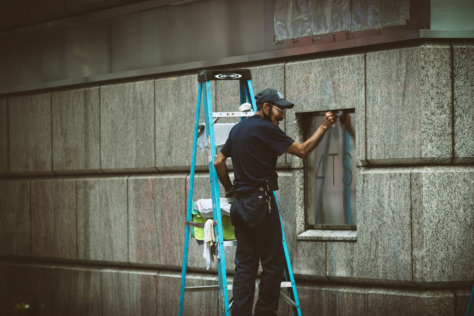 Technician on a ladder installing security equipment on a building wall
