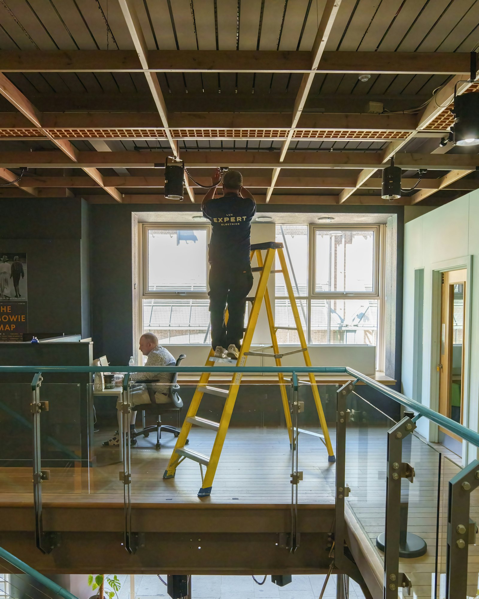 Technician on a ladder working on office ceiling equipment
